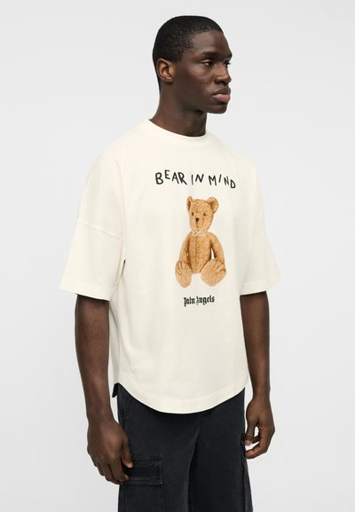 Κρεμ υπερμεγέθη μπλούζα με γραφικό καφέ αρκουδάκι και το κείμενο «BEAR IN MIND». Κατασκευασμένη από βαμβάκι, με κοντά μανίκια και άνετη εφαρμογή.