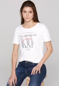 Camiseta blanca de algodón con cuello redondo, que presenta el texto gráfico en negro y rojo "Navega hacia el atardecer" y acentos de patrones abstractos.