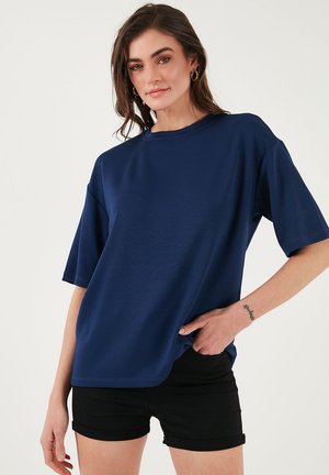 T-shirt oversize blu navy, maniche corte, scollo rotondo, texture liscia, abbinato a pantaloni corti neri. Caratterizzato da linee pulite e un design minimale.