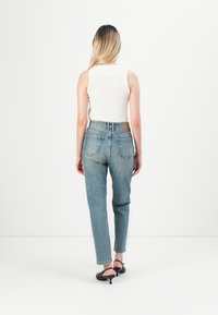 Lichtblauwe high-waisted jeans met een rechte pijp en een rafelige zoom, met een bruine leren label aan de achterkant en twee achterzakken.