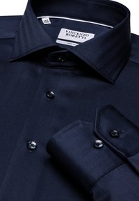 Donkerblauw overhemden met een herringbone textuur, kreukvrij materiaal en zwarte knopen. Voorzien van een spread collar en contrasterende manchetdetails.