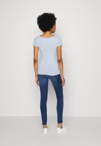 Camiseta ajustada de color azul claro con mangas cortas, combinada con jeans ajustados azul oscuro y zapatillas blancas. Diseño simple, textura suave.