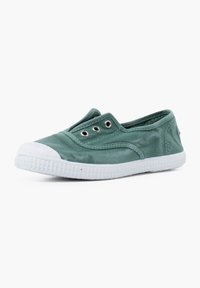 Zapato slip-on de lona verde con suela de goma blanca, que presenta tres ojales metálicos y una textura suave. Diseño simple y de perfil bajo.