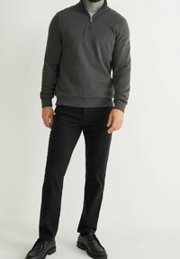 Pull gris à fermeture éclair en matériau doux, associé à un pantalon noir et des chaussures noires. Design simple avec une coupe moderne.