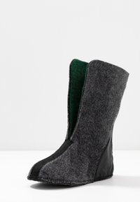 Doublure haute de botte en feutre gris avec semelle noire et doublure intérieure verte visible, debout sur une surface blanche.