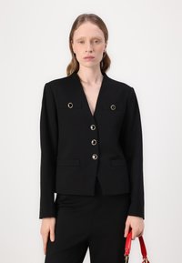 Mustmust suit, mille sügava V-kaelusega, kuus dekoratiivset nööpi, millel on erinevad kivid, kaks esi-taskut ja pikad varrukad.