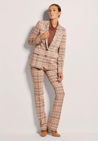 Geruit pak in zachte stoffen; roze, bruin en crème tinten; gestructureerde blazer met opstaande revers; getailleerde broek; soepele textuur.