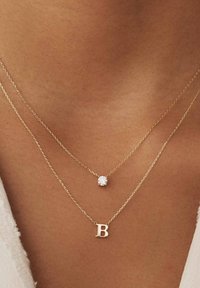 Goldschichtige Halsketten mit einem runden Diamantanhänger und einem Buchstaben "B" Charm, die zarte Ketten und polierte Oberflächen zeigen.