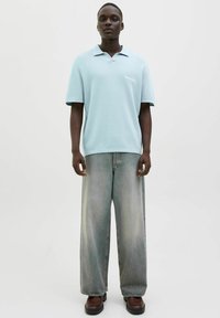 Lysblå kortærmet polo t-shirt med løs pasform, parret med brede blege denimjeans og brune kraftige støvler.