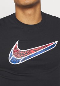 Camiseta negra con un gran logo de Nike en blanco, con patrones de estampado animal en rojo y azul integrados en el diseño.