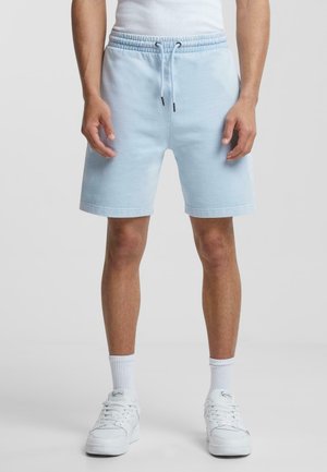 Light blue cotton shorts with an elastic waistband, drawstring detail, and side pockets. Styled with white sneakers and ankle socks.