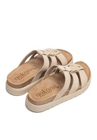 Sandalias de gamuza beige con correas cruzadas, plantilla acolchada, mediado de corcho y suela de goma. Presentan un pequeño acento metálico en las correas.