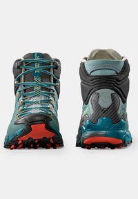 Scarpe da trekking teal e nere con tomaia testurizzata, lacci vivaci, suola in gomma resistente e dettagli rossi sulla suola.