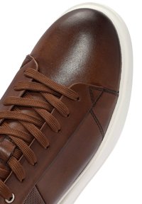 Sneaker in pelle marrone con punta arrotondata, lacci tono su tono, design elegante, suola in gomma bianca a contrasto e dettagli di cucitura discreti.