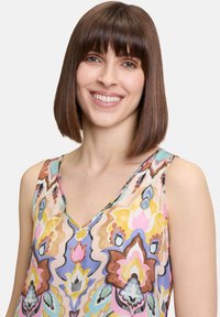 Haut sans manches multicolore avec un col en V, présentant des motifs floraux et abstraits dans des teintes de rose, jaune, violet et marron. Texture de tissu lisse.