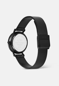Montre avec un bracelet en maille noire et un boîtier rond noir. Équipée d'un fond en métal argenté, d'une boucle proéminente et de détails texturés subtils sur le bracelet.