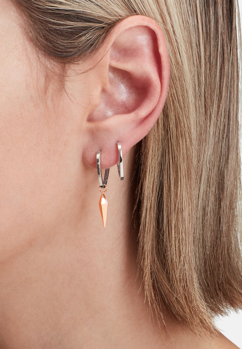 Boucle d'oreille en argent avec un long pendentif en cuivre poli, suspendu à un fin maillon. Gros plan sur le détail de l'oreille.