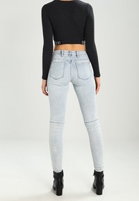 Jeans ajustados de cintura alta, en un tono azul claro con un acabado desvanecido, cinco bolsillos y una abertura de pierna estrecha, combinados con un top negro de corte corto.