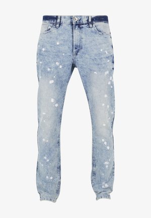 Jean en denim bleu clair avec effet usé, présentant des éclaboussures de peinture blanche, un design classique à cinq poches et une braguette à boutons.