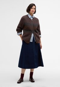 Bronze ribbed cardigan with a zip front, layered over a light blue striped shirt. Paired with a dark denim midi skirt and brown loafers.