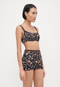 Svart blomstret bikini med oransje og hvite mønstre. Toppen har justerbare stropper; de høytalttede buksene har en teksturert midjebånd.