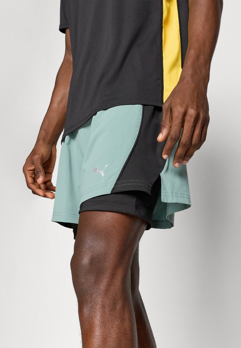Camisa atlética negra y amarilla; pantalones cortos negros y verde claro con aberturas laterales y un pequeño logo blanco. Textura suave, diseño hasta la rodilla.