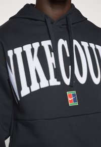 Črna kapuca z veliko belim napisom "NIKE", teksturirano blago in barvno Nike oznako na sprednji strani.
