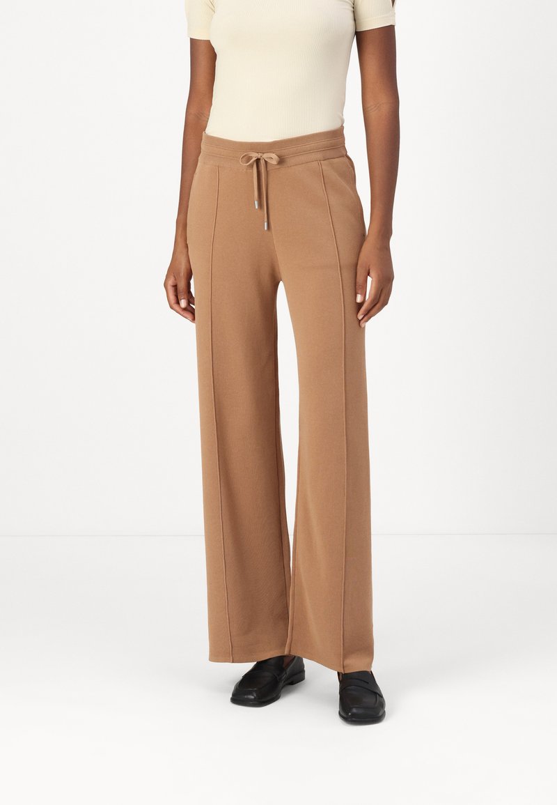 Pantaloni a gamba larga in un morbido tessuto beige con vita regolabile e dettagli delle cuciture a contrasto. Abbinati a scarpe nere per un look informale.