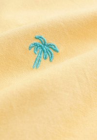 Tejido amarillo con una superficie texturizada que presenta un diseño bordado de una palmera azul en una esquina.