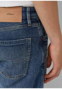 Ciemnoniebieskie dżinsy o fakturowanej powierzchni, z pomarańczowymi przeszyciami, skórzaną naszywką na pasku oraz tylną kieszenią.