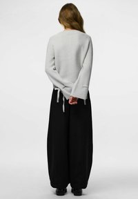 Hele halli soonikko, millel on pikad varrukad ja sidumisrihmad; koos laiad mustad püksid; pehme tekstuur ja vabalt istuv lõige.