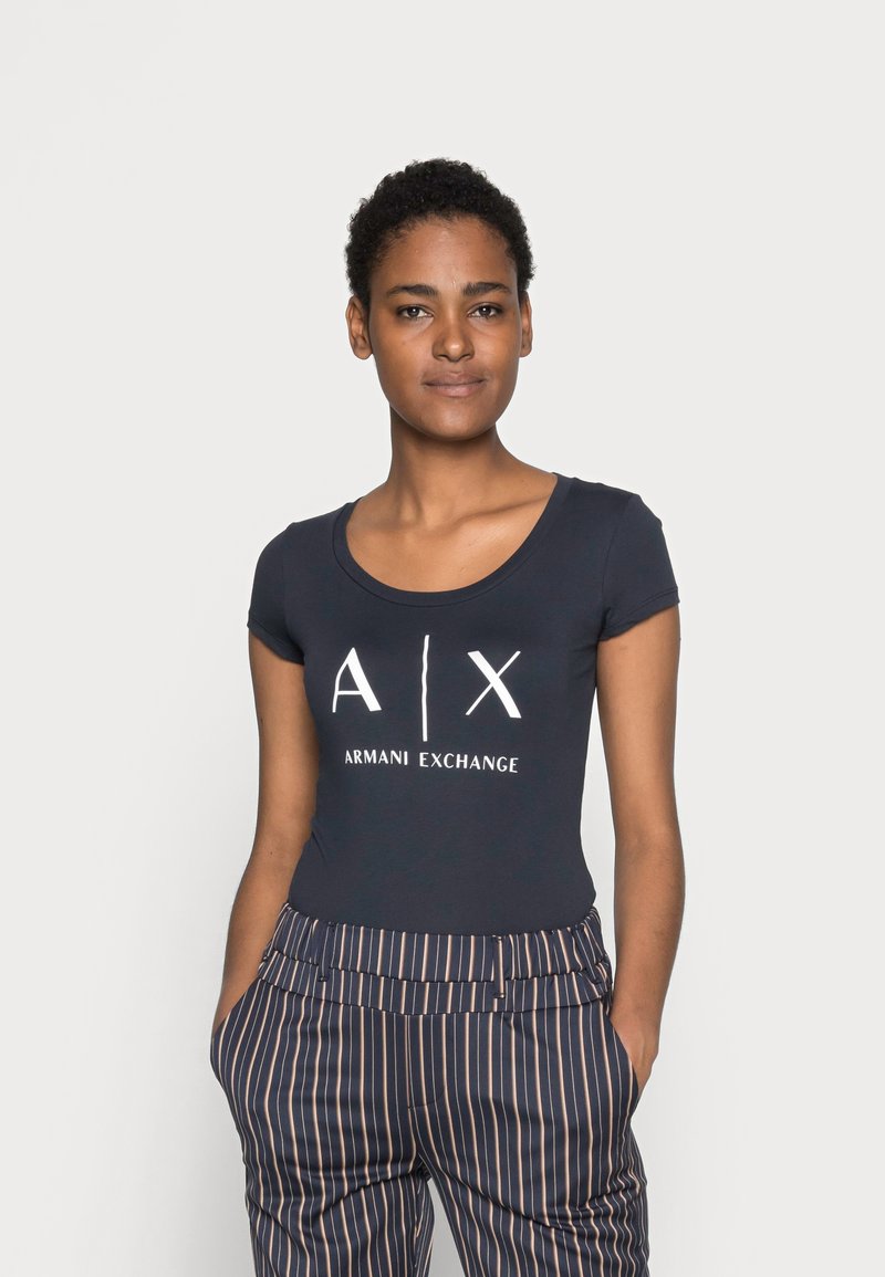 T-shirt azul-marinho de manga curta com o logotipo branco "A/X ARMANI EXCHANGE", combinado com calças de cintura alta plissadas com riscas.