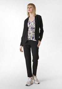 Svart figursydd kavaj över en blommig topp i lila och creme, tillsammans med svarta smala byxor och beige sneakers med vita detaljer.