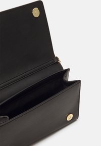 Svart läderhandväska med en slank design, utrustad med en guldfärgad knappstängning och en rymlig insida med en extra ficka för bättre organisering.