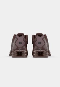 Brown athletic shoes with a glossy finish, mesh upper, padded collar, and textured sole featuring air cushioning for support.