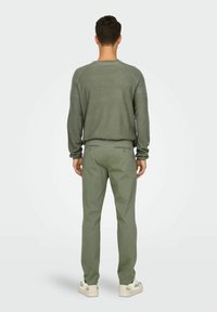 Pull en maille gris-vert clair avec un motif texturé, associé à un pantalon tailleur assorti. Des baskets décontractées complètent la tenue.