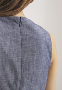 Top sin mangas de chambray azul, con una textura sutil y una cremallera oculta en la parte posterior, que resalta un diseño limpio y ajustado.