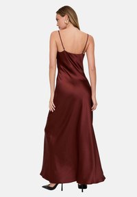 Maxikleid aus burgunderfarbenem Satin mit dünnen Trägern, glatter Textur und fließender Silhouette, mit tief ausgeschnittener Rückenpartie. Schwarze High Heels sichtbar.