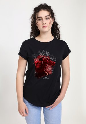 Sort bomulds T-shirt med et rødt grafik af en karakter i en actionstilling, med hvide og røde baggrundsdetaljer. Korte ærmer, afslappet pasform.