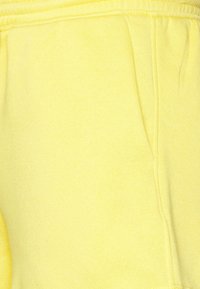 Pantalon de survêtement jaune en mélange de coton doux, doté d'une ceinture élastique et d'une poche latérale, avec une texture lisse et un design décontracté.