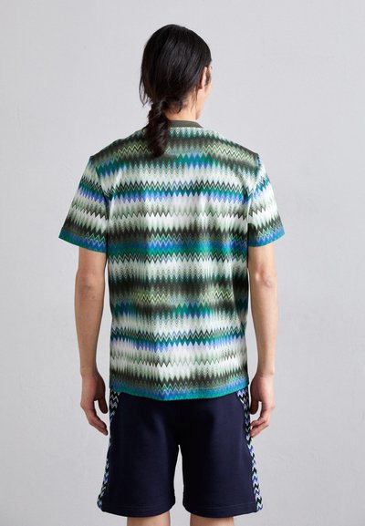Chemise à manches courtes avec un motif en zigzag en vert, bleu et blanc, dotée d'une encolure ronde et d'une coupe décontractée, associée à un short bleu marine.