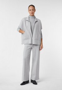 Giacca grigia con zip e tasche, abbinata a pantaloni larghi coordinati. Entrambi realizzati in tessuto morbido con un dolcevita a coste sotto.