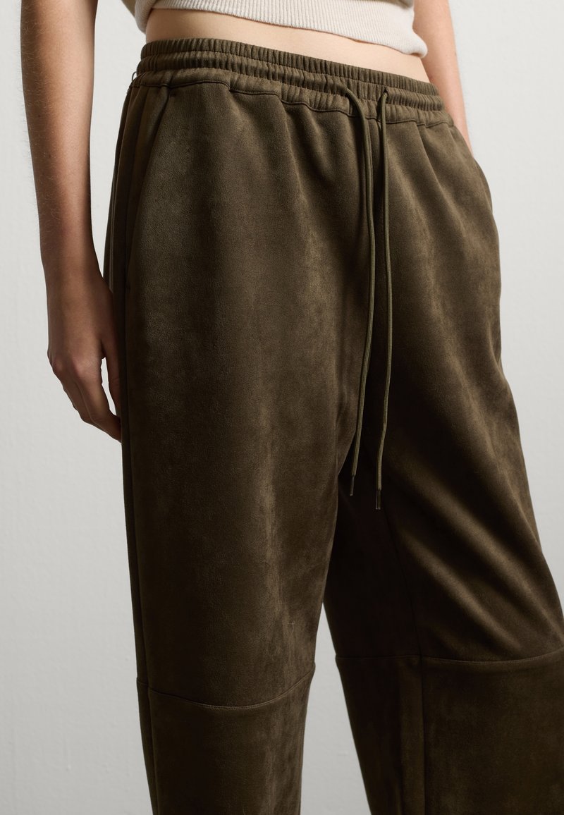 Weiche, olivgrüne Jogginghosen aus einem samtähnlichen Stoff. Mit einem elastischen Bund und Kordelzügen sowie seitlichen Taschen. Glatte Oberfläche überall.