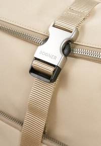 Béžová textilná taška s výrazným strieborným uzáverom s nápisom "BOGNER", doplnená elegantným zipsovým detailom a textúrovanými popruhmi.