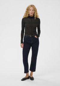 Must mustaga pikkade varrukatega särk kõrge kaelusega, koos tumepruunide sirgete teksade ja mustade lamedate kingadega. Lihtne disain, sile tekstuur.