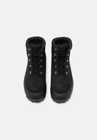 Melnas ūdensizturīgas potītes ar zamša virsu, gumijas zoli, sešiem metāla acu caurumiem un auklām. Teksturēta virsma un polsterēta apkakle.