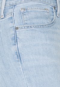 Jeans de denim azul claro que presentan un primer plano de la textura de la tela, costuras visibles y un pequeño detalle del bolsillo trasero.