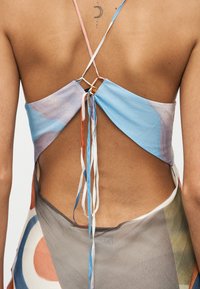 Πίσω όψη πολύχρωμου υφασμάτινου τοπ με τριγωνικό σχέδιο, λεπτές τιράντες και ρυθμιζόμενους δεσμούς σε αποχρώσεις του μπλε, ροζ και πορτοκαλί.