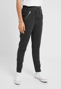 Kolgrå joggerbyxor i mjukt material, med dragkedjefickor på sidorna, elastisk midja och avsmalnande ben, tillsammans med vita sneakers.