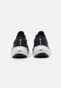 Baskets de course noires et grises avec une tige en maille, semelle intermédiaire blanche et semelle extérieure noire à motifs. Présente un logo sur le talon et sur le côté.